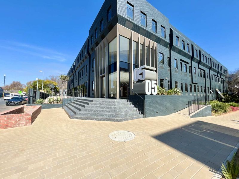 Modern office building exterior featuring a dark brick facade, glass entrance, and paved approach with architectural signage.