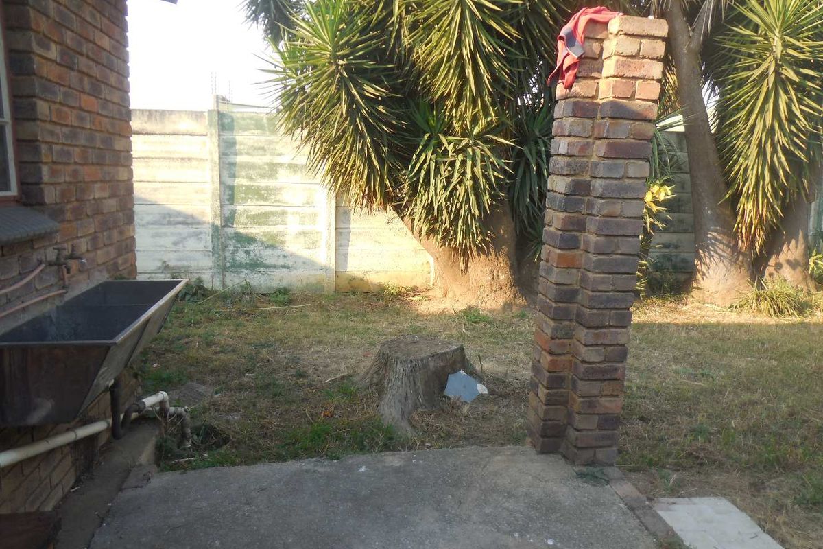 Rear garden area featuring a concrete patio, brick pillar, and utility sink, set against a precast concrete boundary wall.