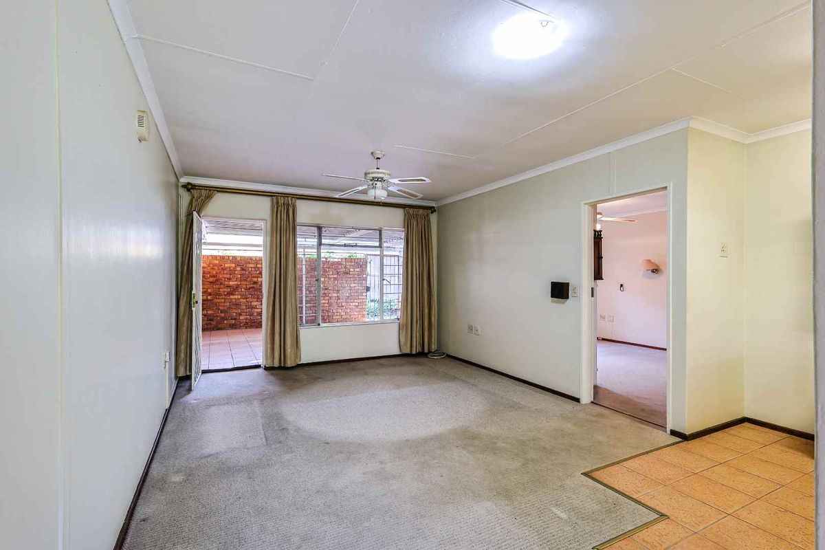 A spacious living area featuring neutral carpeting, a ceiling fan, and direct access to a private patio through a glass door.