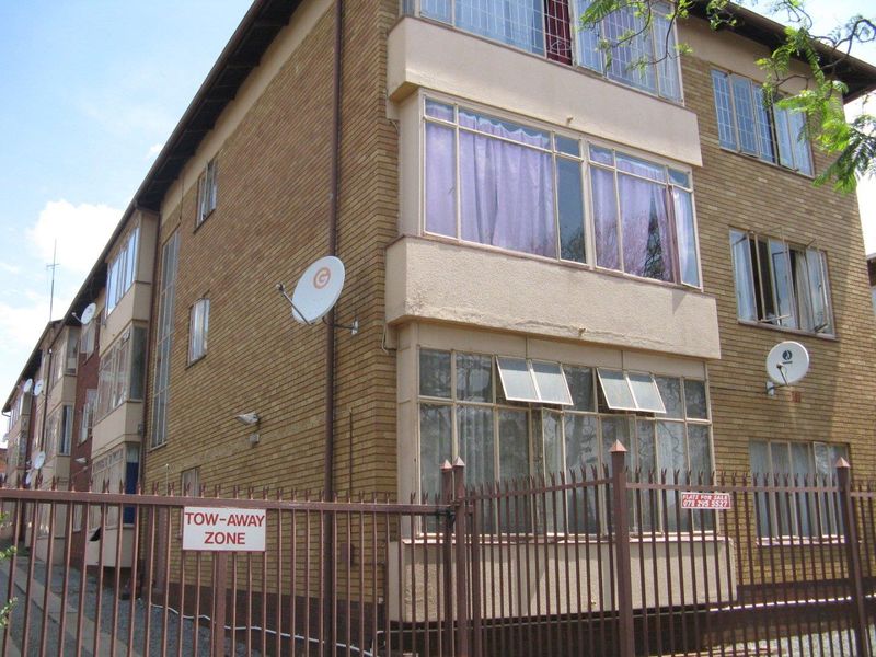 Exterior view of a multi-story brick apartment building featuring metal security fencing and multiple satellite dishes installed on the facade.