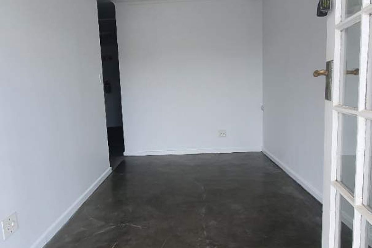 A bright, empty office space featuring polished concrete flooring, recessed lighting, and a classic French door entrance.