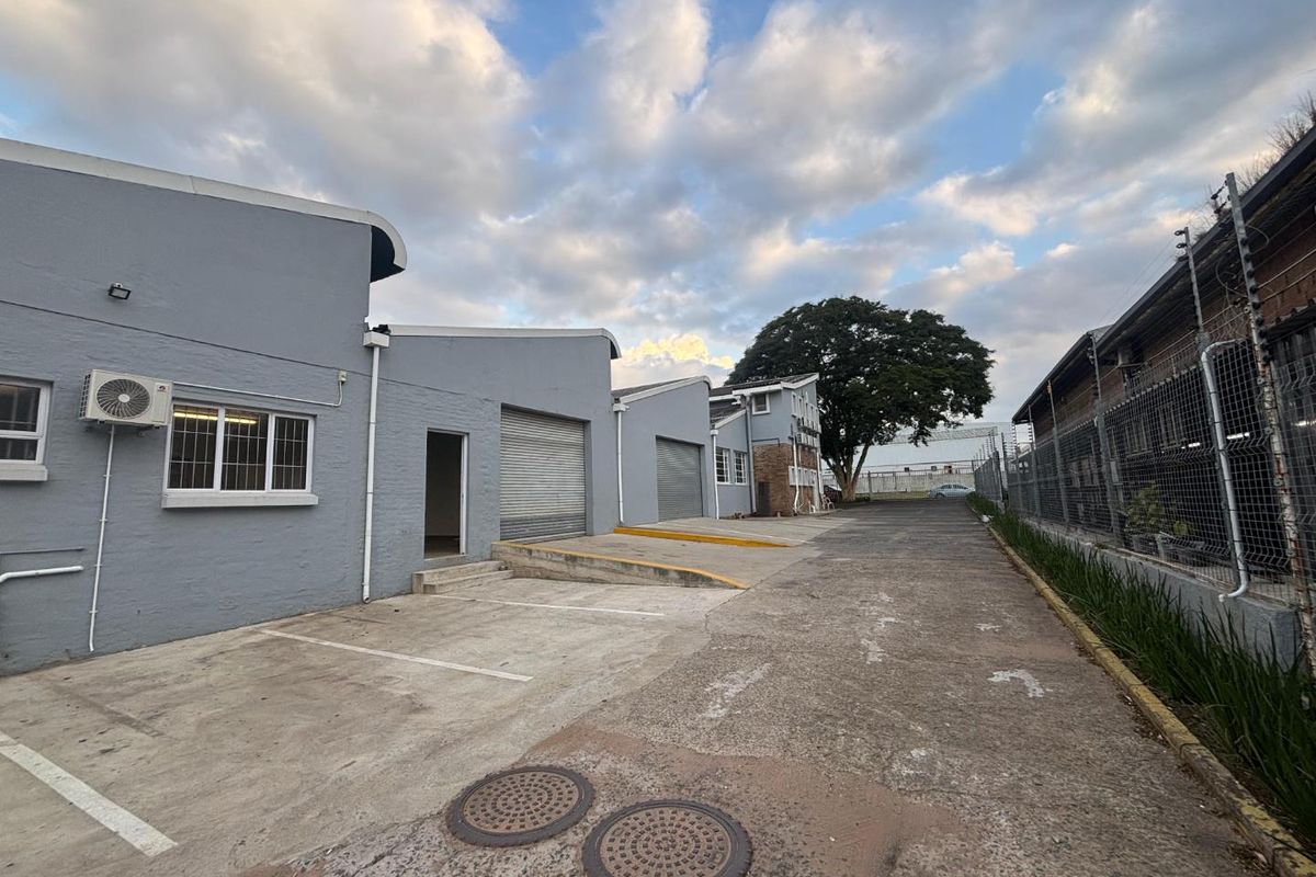 Exterior view of an industrial property featuring concrete loading bays, roller shutter doors, and perimeter security fencing.