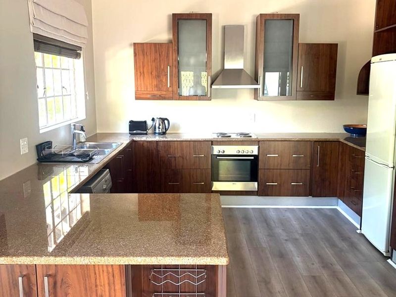 Modern kitchen featuring dark wood cabinetry, granite countertops, stainless steel appliances, and a vaulted ceiling with laminate flooring.