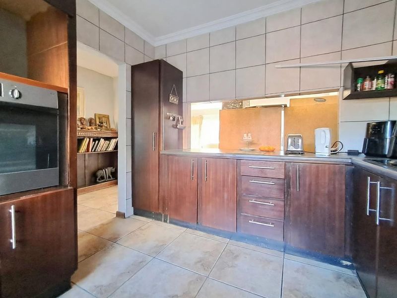 A functional kitchen featuring dark wood cabinetry, built-in oven, tiled splashbacks, and a convenient pass-through window connecting to the adjacent living area.