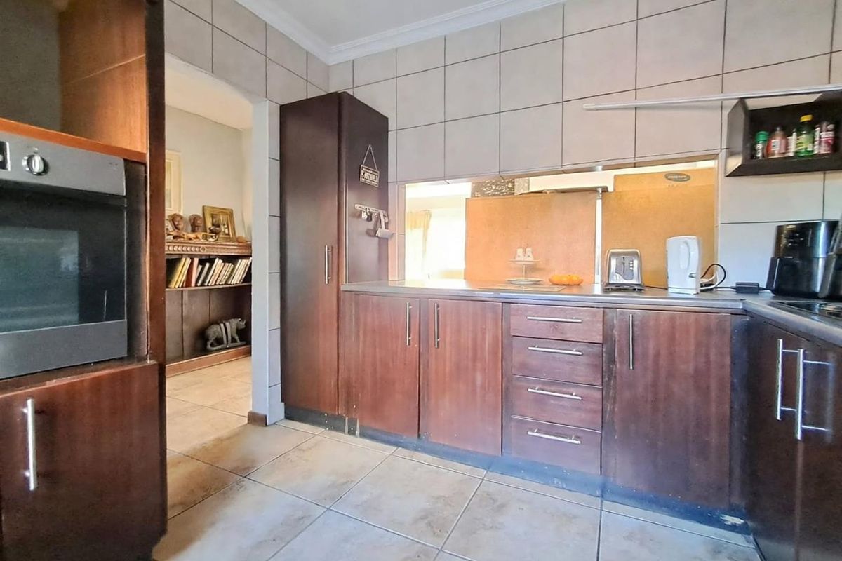 A functional kitchen featuring dark wood cabinetry, built-in oven, tiled splashbacks, and a convenient pass-through window connecting to the adjacent living area.