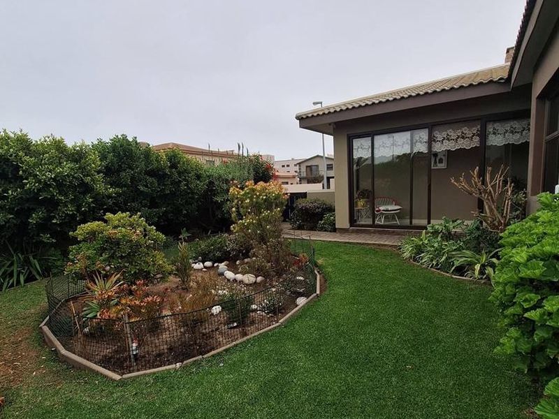 A well-maintained rear garden featuring a manicured lawn, landscaped garden beds, and sliding glass door access to the home.