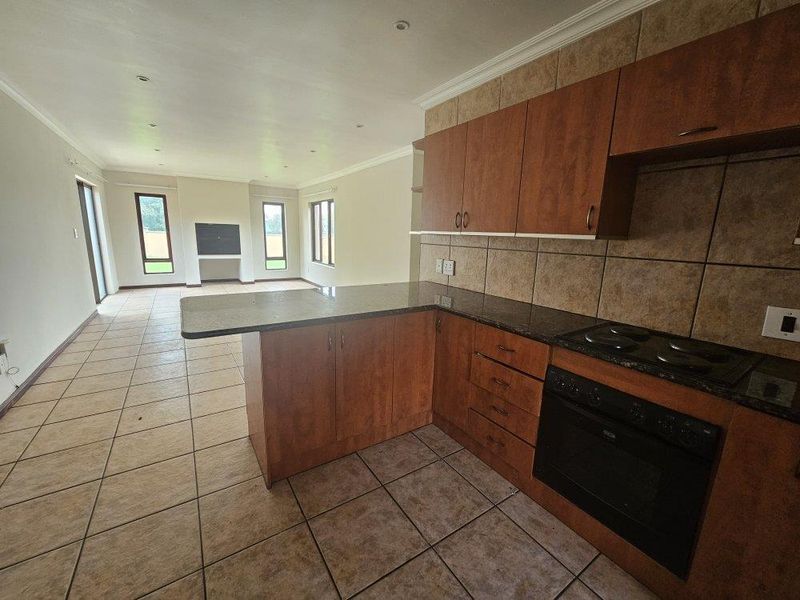 Open-plan kitchen and living area featuring tiled flooring, built-in wooden cabinetry, granite countertops, and integrated oven and hob.