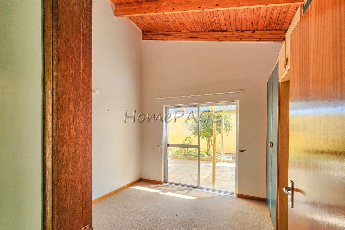A bedroom featuring a high timber-beamed ceiling, built-in cupboards, and a sliding glass door providing direct access to the rear patio.
