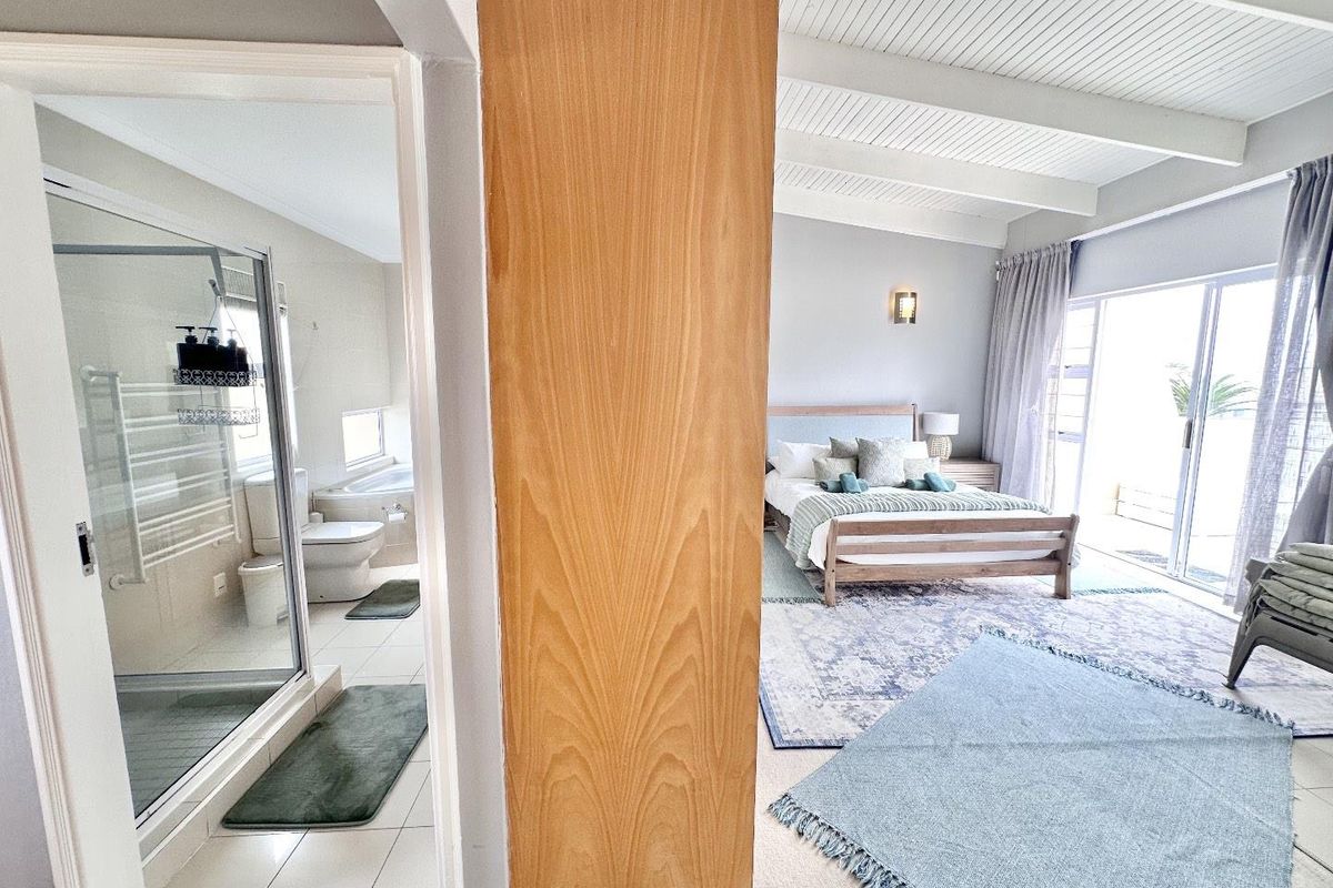A spacious bedroom featuring a vaulted ceiling and an en-suite bathroom with a glass-enclosed shower and tiled flooring.