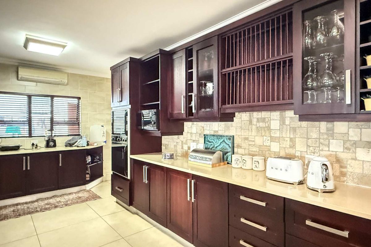 A well-appointed kitchen featuring dark wood cabinetry, stone-tiled backsplash, integrated oven, and light-colored stone countertops with ample storage space.