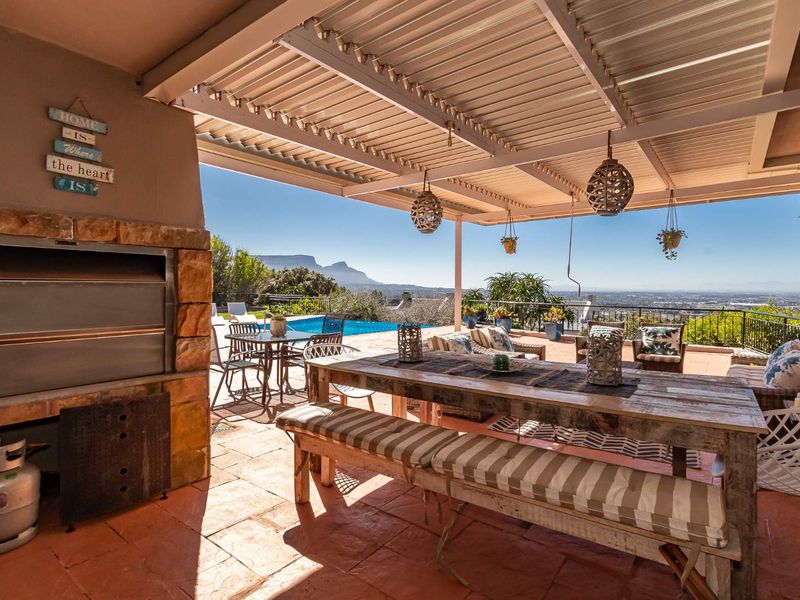 Spacious covered patio featuring a built-in braai with stone cladding, overlooking the swimming pool and scenic mountain views.