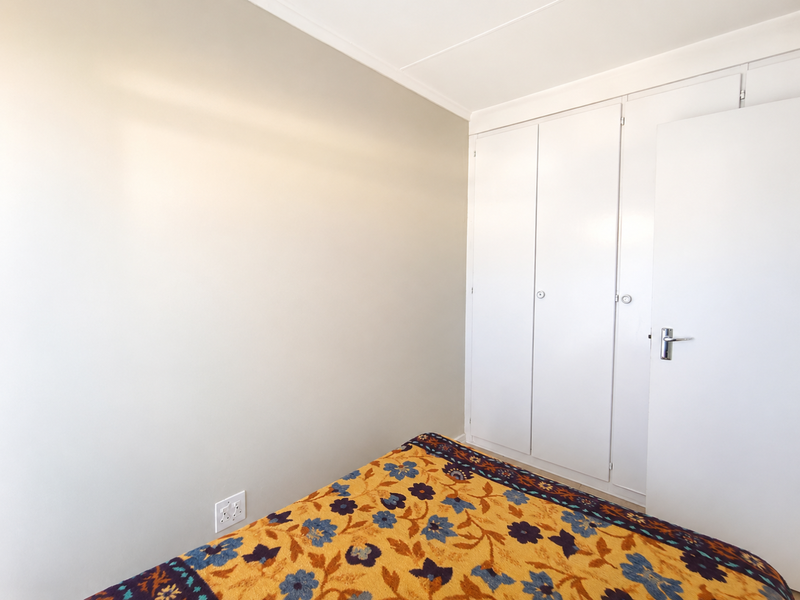 A clean, neutral bedroom featuring a built-in wardrobe and standard electrical fixtures, offering a blank canvas for personalization.