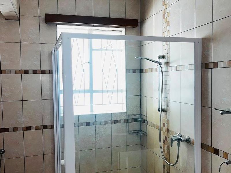 A functional bathroom featuring a glass-enclosed shower, tiled walls with decorative accents, and a vanity countertop.