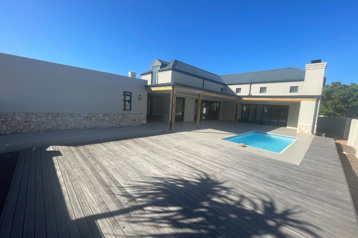 Spacious rear exterior featuring a large timber deck, swimming pool, and a covered patio area attached to the main residence.