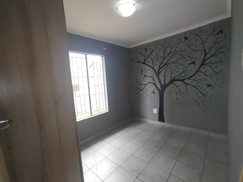 A vacant bedroom featuring tiled flooring, a window with security bars, and a decorative tree mural on the feature wall.