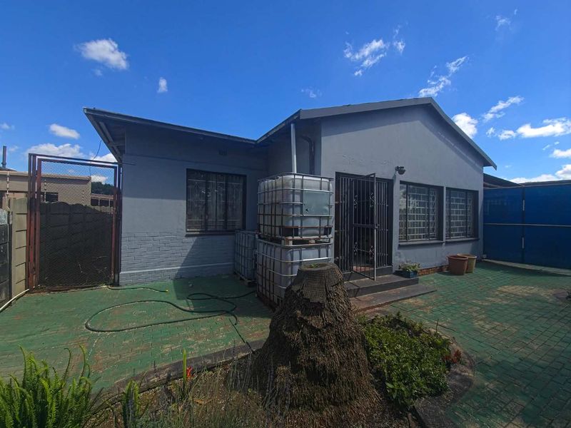 Rear exterior view of the house featuring a paved patio area, security gates, burglar bars, and external water storage tanks.