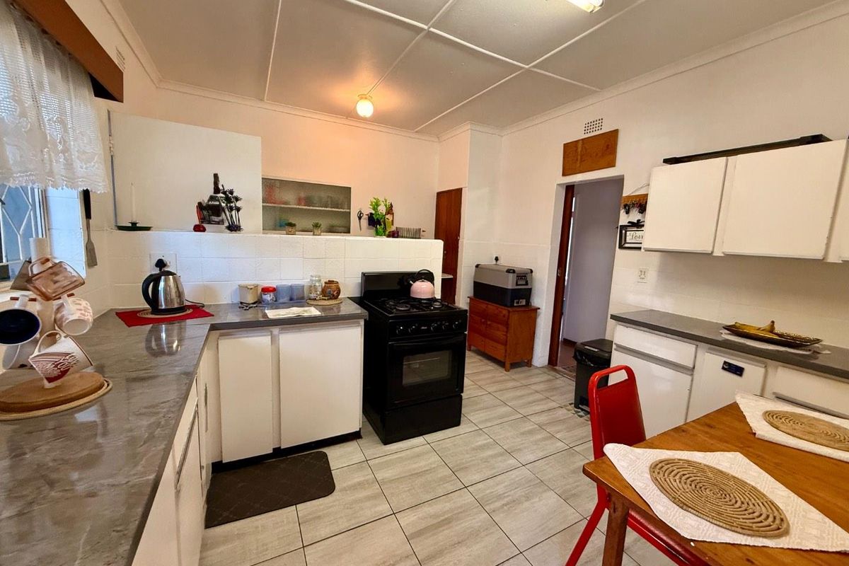 A functional kitchen featuring tiled flooring, laminate countertops, white cabinetry, and a freestanding stove, offering a practical layout for daily meal preparation.