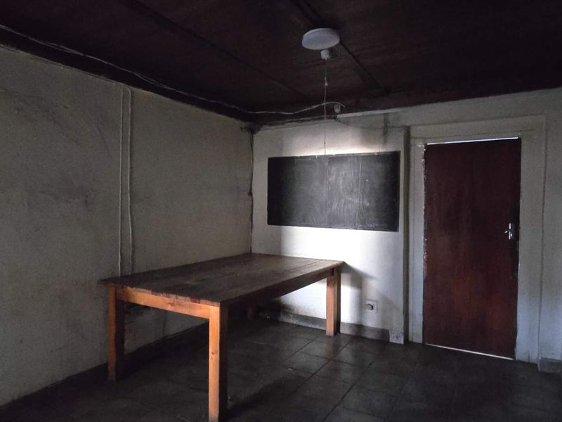 A sparse utility space featuring tiled flooring, a timber ceiling, and security bars on the window, currently in need of cosmetic refurbishment.