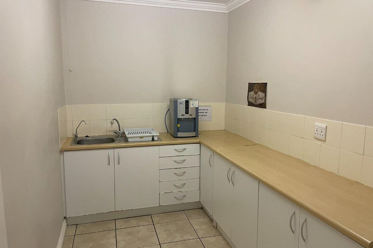 A functional office kitchenette featuring white cabinetry, laminate countertops, a stainless steel sink, and tiled splashbacks.