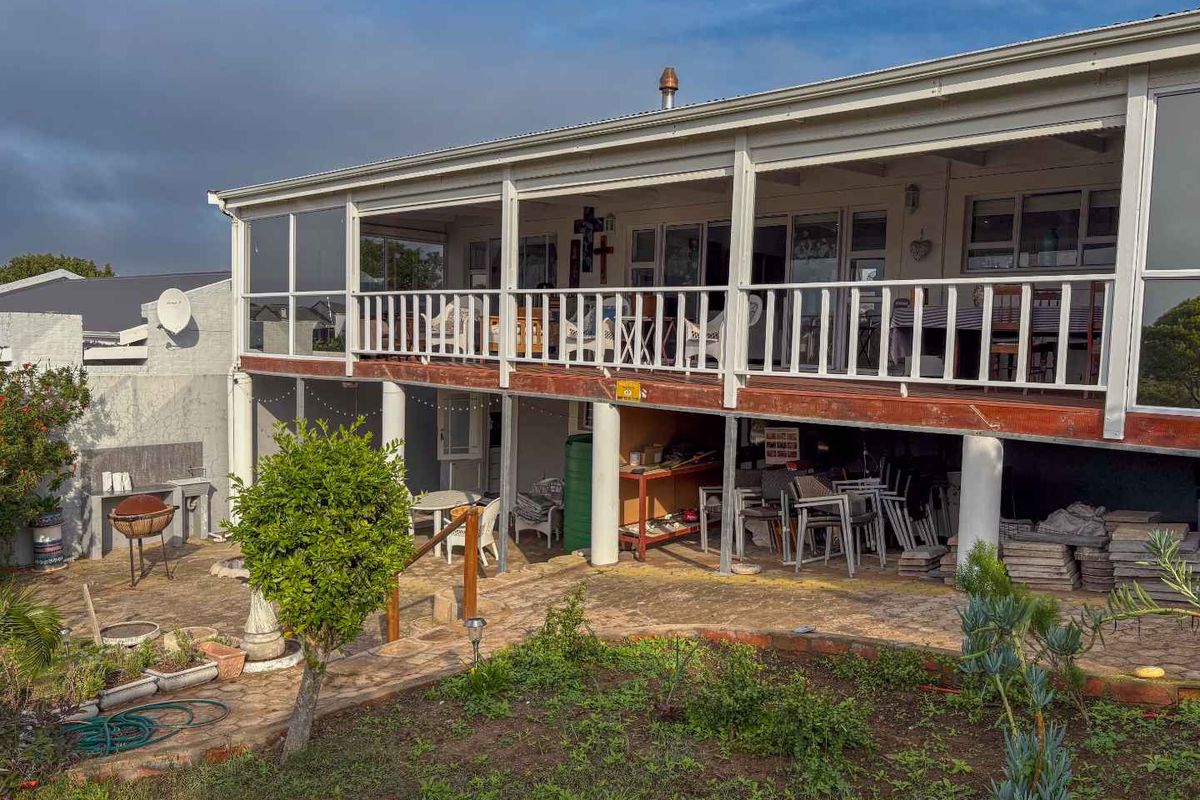 Rear view of the property featuring an elevated timber deck with balustrades, overlooking a paved patio area and garden space.