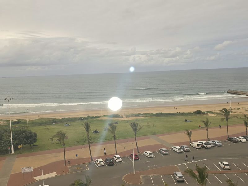 A scenic elevated view overlooking the coastline, beach, and public parking area.