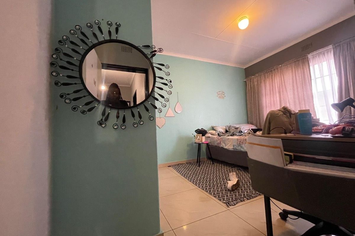 A bedroom featuring tiled flooring, a light-colored accent wall, and a window with curtains, providing a functional living space.