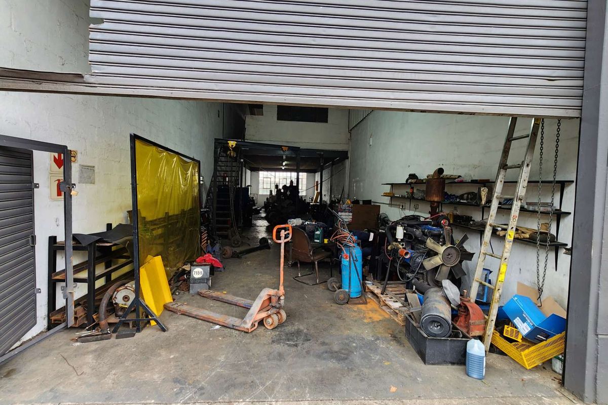 Industrial workshop space featuring a large roller shutter door, concrete flooring, and built-in steel shelving units suitable for mechanical or storage operations.