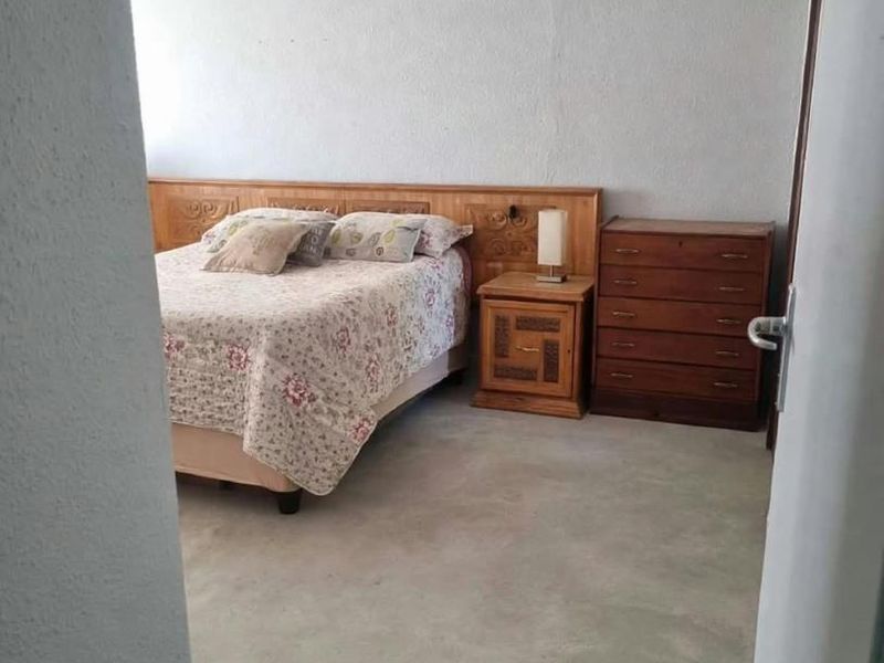 A bedroom featuring a built-in wooden headboard, recessed ceiling lighting, and unfinished concrete flooring, offering potential for renovation and modern flooring installation.