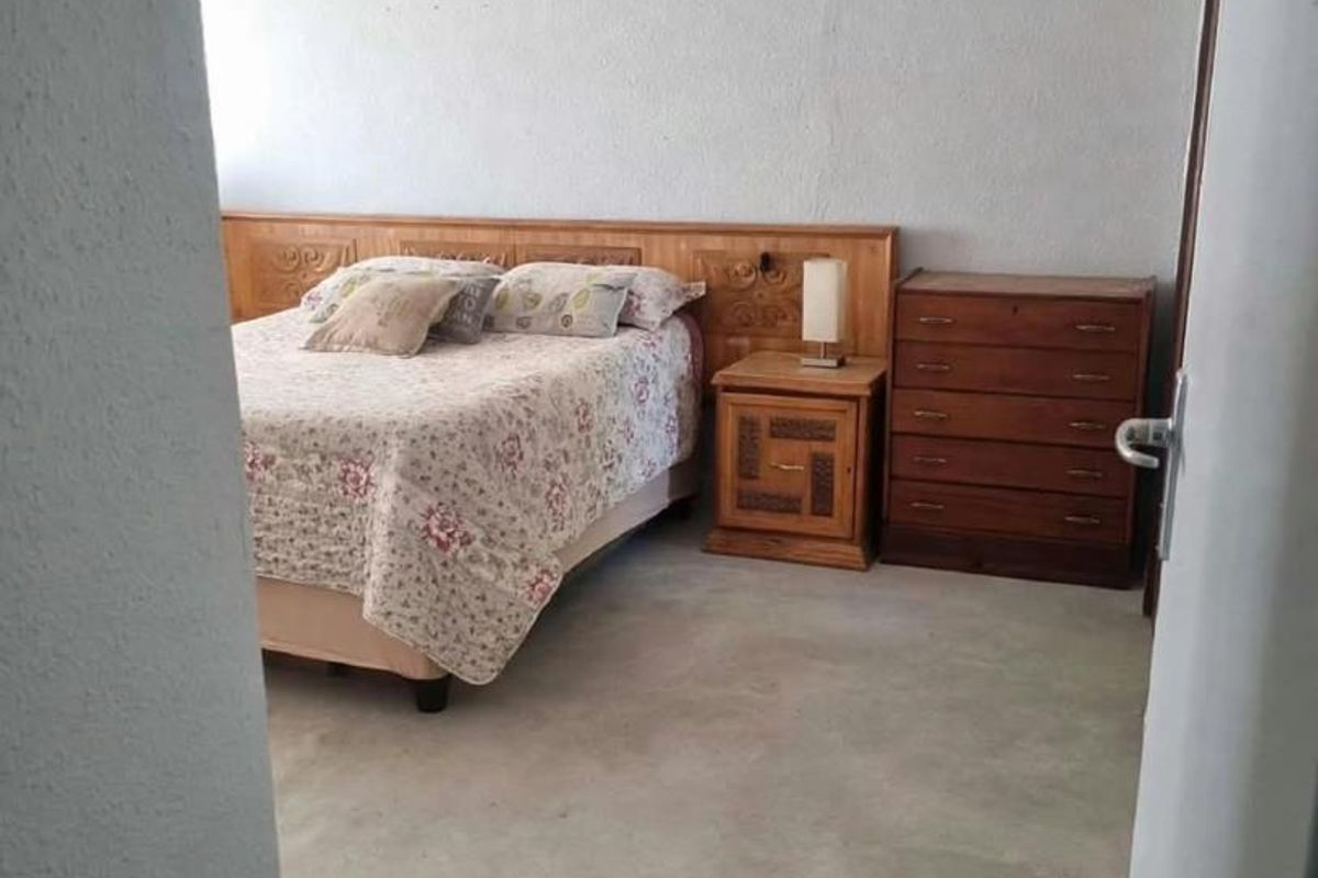 A bedroom featuring a built-in wooden headboard, recessed ceiling lighting, and unfinished concrete flooring, offering potential for renovation and modern flooring installation.