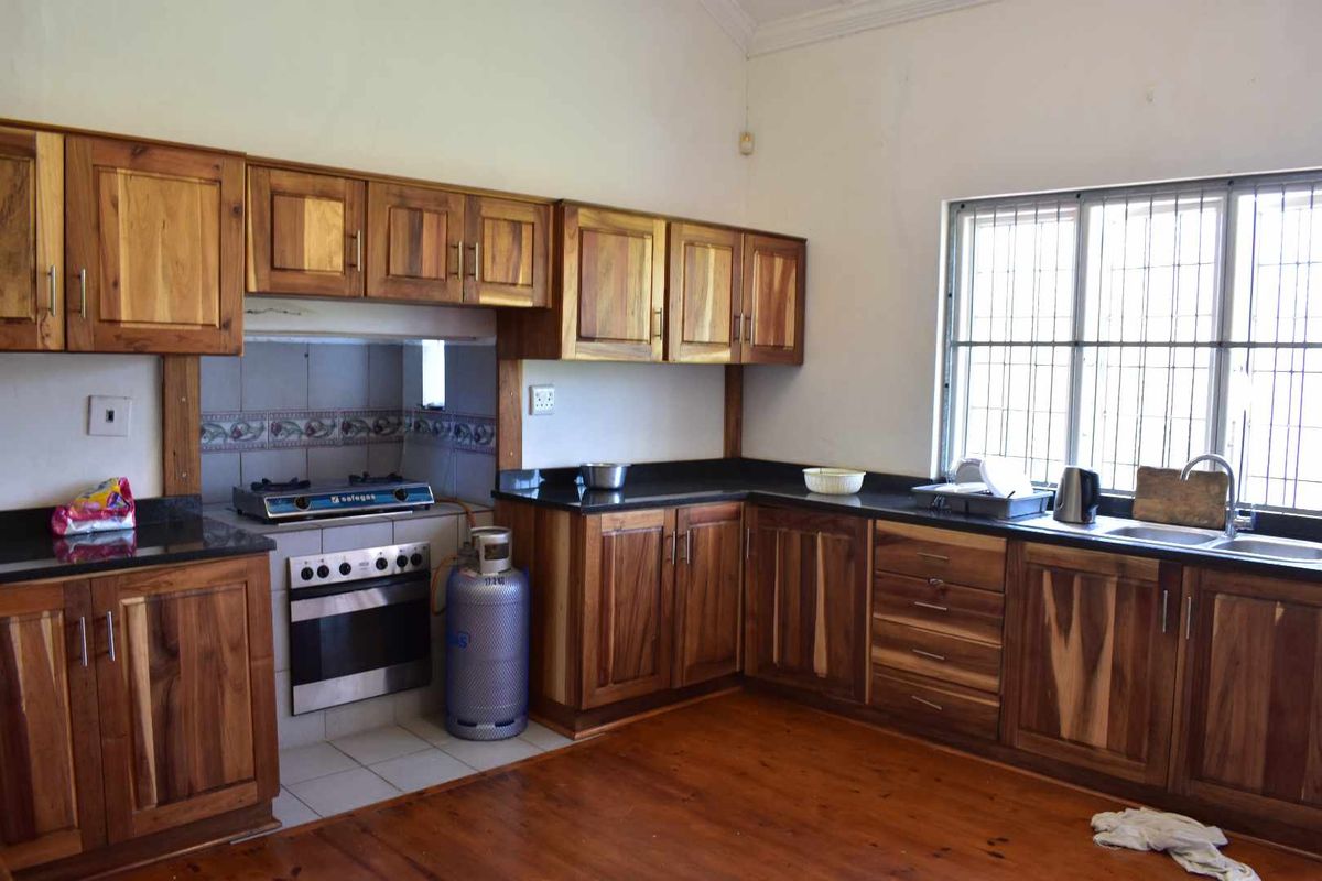 A functional kitchen featuring solid wood cabinetry, dark granite countertops, a built-in oven with gas hob, and polished wooden flooring.