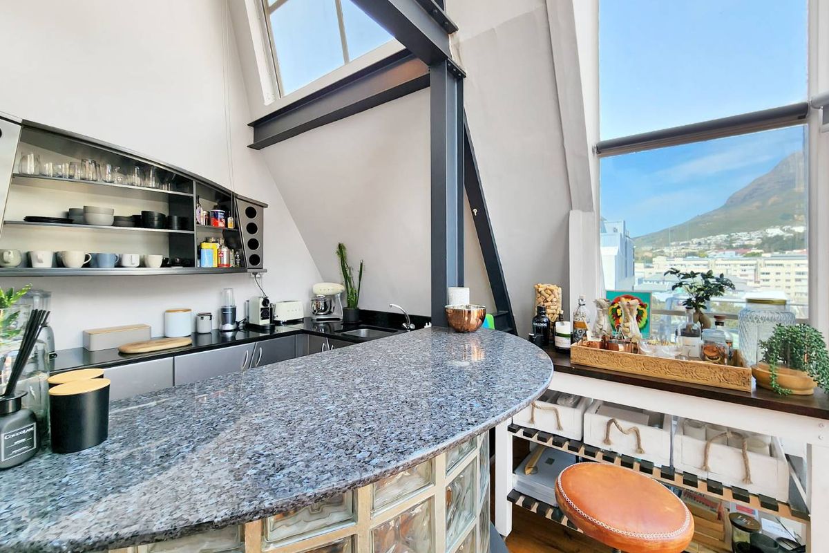 Modern kitchen area featuring a granite breakfast bar, glass block base, open shelving, and large windows with mountain views.