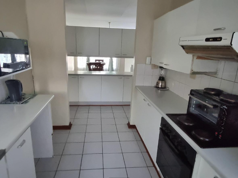 A functional kitchen featuring white built-in cabinetry, laminate countertops, tiled backsplash, and integrated cooking appliances with ceramic tile flooring throughout.