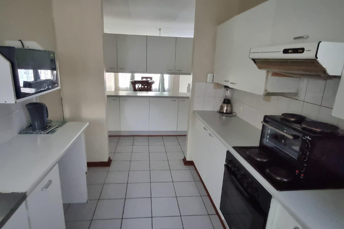 A functional kitchen featuring white built-in cabinetry, laminate countertops, tiled backsplash, and integrated cooking appliances with ceramic tile flooring throughout.