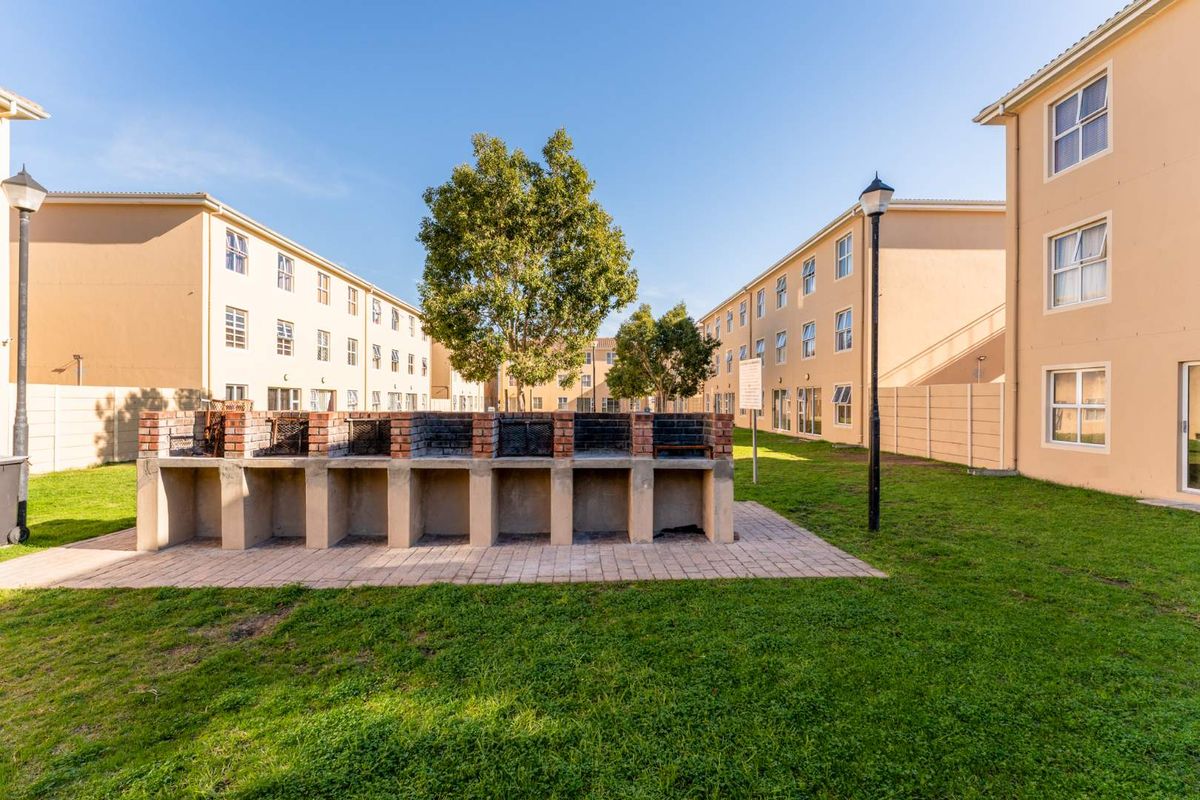 Communal outdoor area featuring a multi-bay brick built-in braai facility set within a landscaped apartment complex courtyard.