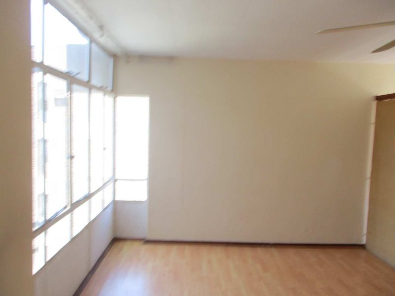 An empty living room featuring laminate flooring, a ceiling fan, and large windows that provide ample natural light.