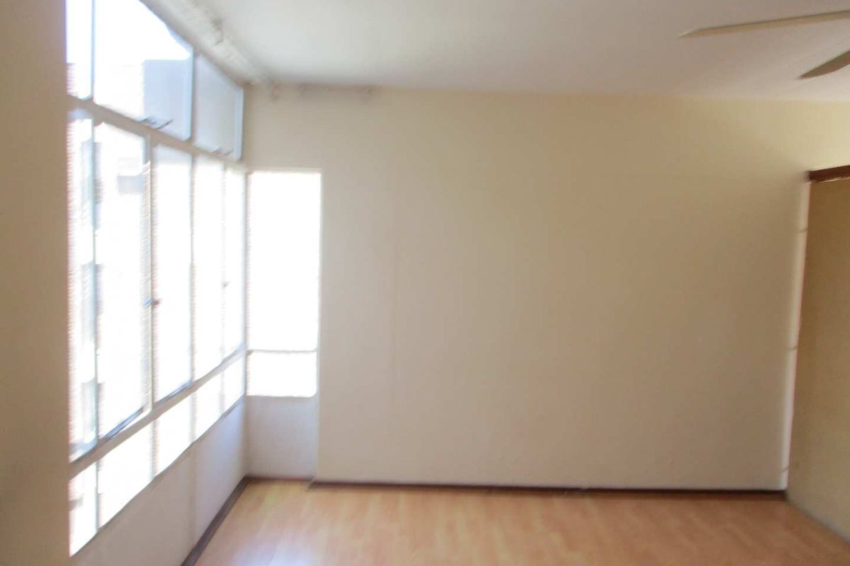 An empty living room featuring laminate flooring, a ceiling fan, and large windows that provide ample natural light.