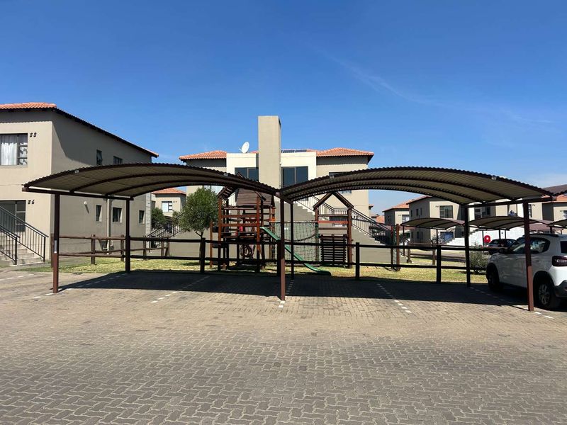 A communal paved parking area featuring covered carports and an adjacent outdoor playground within a townhouse complex.