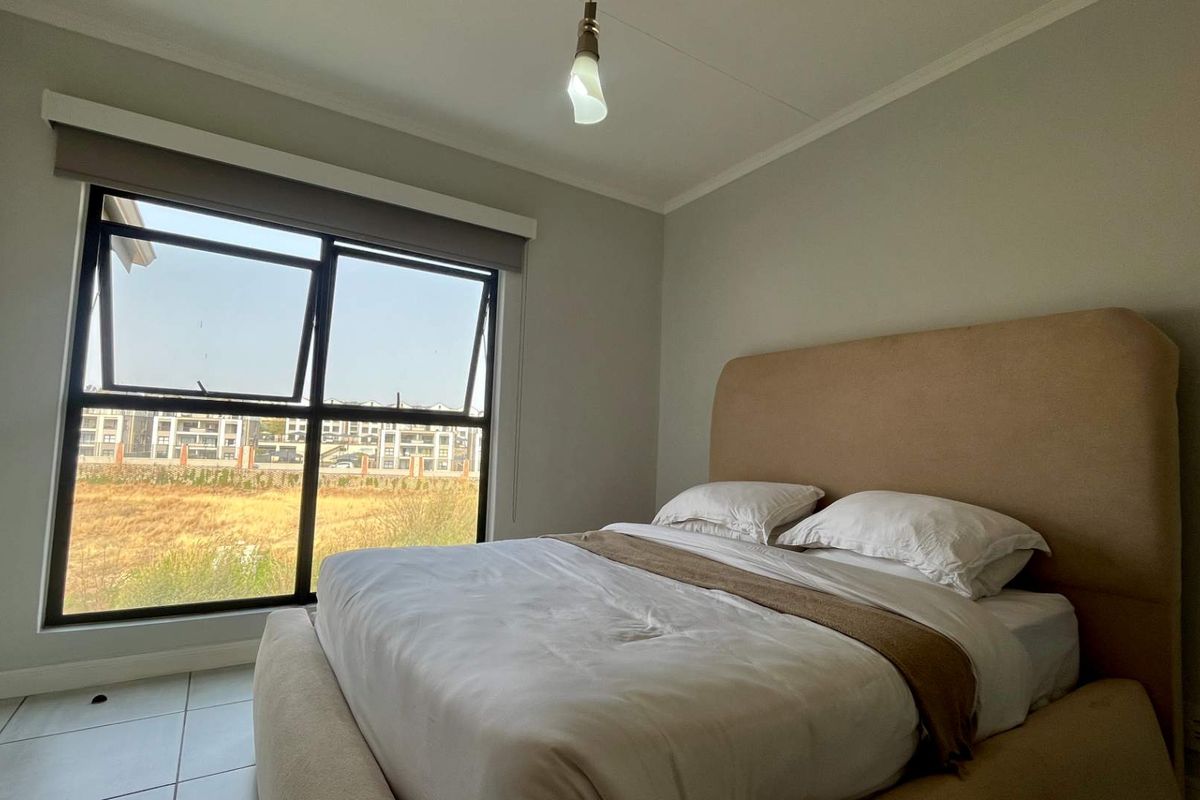A bright bedroom featuring tiled flooring, a large aluminium window with a roller blind, and neutral wall finishes.