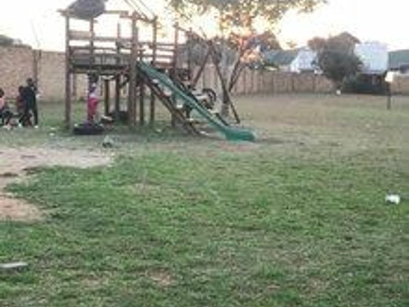 A large outdoor garden area featuring a perimeter brick wall and a wooden playground structure with a slide.