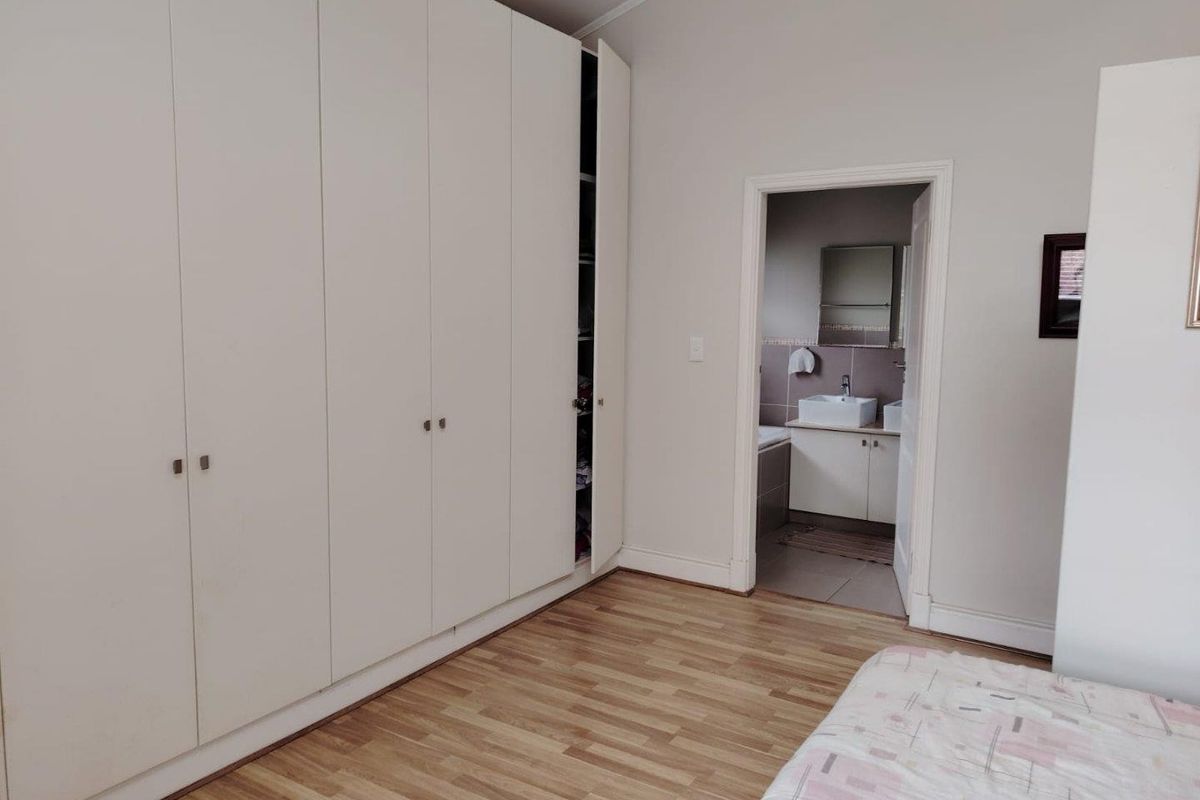 A bedroom featuring built-in cupboards, laminate flooring, and direct access to an en-suite bathroom.