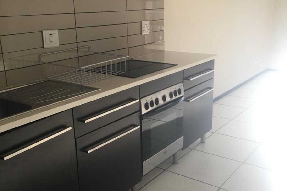 Modern kitchen featuring dark cabinetry, integrated oven and hob, extractor fan, and tiled splashback, offering a clean and functional workspace.