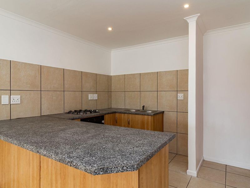 A clean, functional kitchen featuring built-in wooden cabinetry, granite countertops, a gas hob, and neutral tiled splashbacks in an open-plan layout.