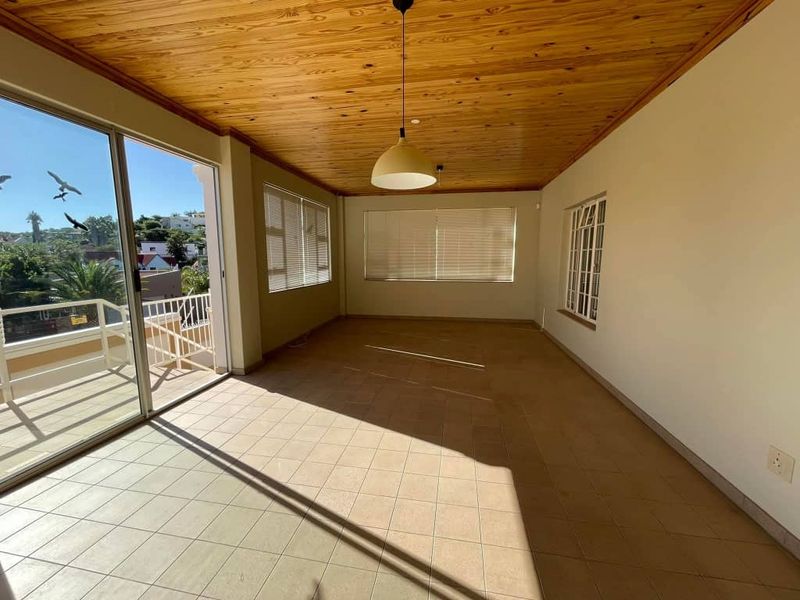 Spacious living area featuring a warm timber ceiling, ceramic tiled flooring, and large sliding doors opening onto a balcony with natural light.