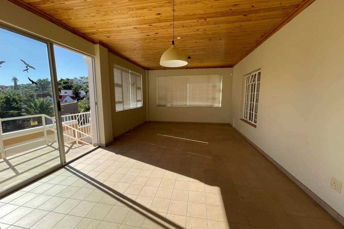 Spacious living area featuring a warm timber ceiling, ceramic tiled flooring, and large sliding doors opening onto a balcony with natural light.