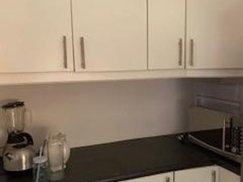 A compact kitchen area featuring white built-in cabinetry and dark laminate countertops, providing functional storage and workspace.