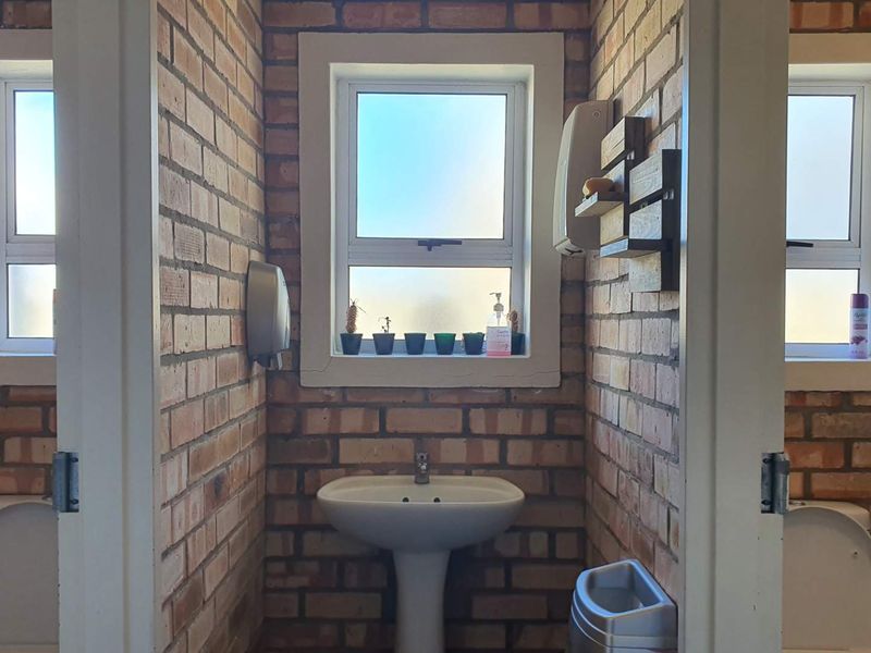 A functional bathroom featuring exposed brick walls, pedestal basin, and multiple toilet cubicles with frosted glass windows for natural light.