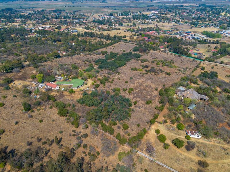 An aerial view of a large residential vacant land plot featuring natural vegetation, existing structures, and surrounding rural landscape.