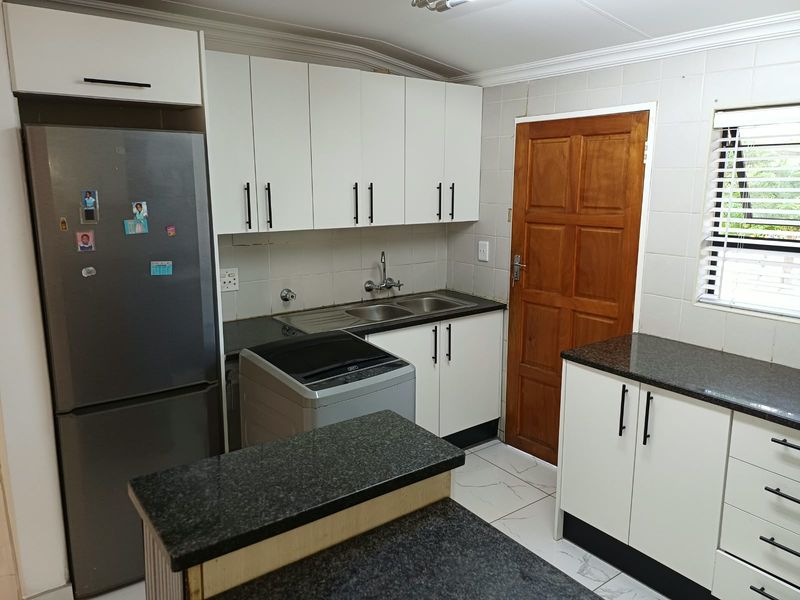 A functional kitchen featuring white cabinetry, dark granite countertops, a double basin sink, and tiled flooring with a convenient layout.