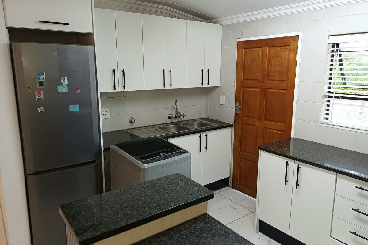 A functional kitchen featuring white cabinetry, dark granite countertops, a double basin sink, and tiled flooring with a convenient layout.
