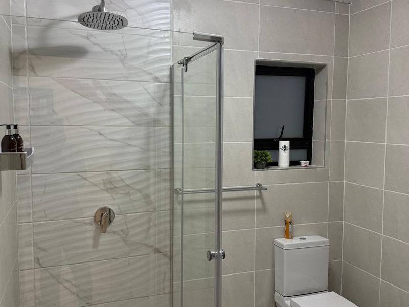 Modern bathroom featuring a walk-in shower with a rain shower head, glass enclosure, and contemporary tiled finishes throughout.